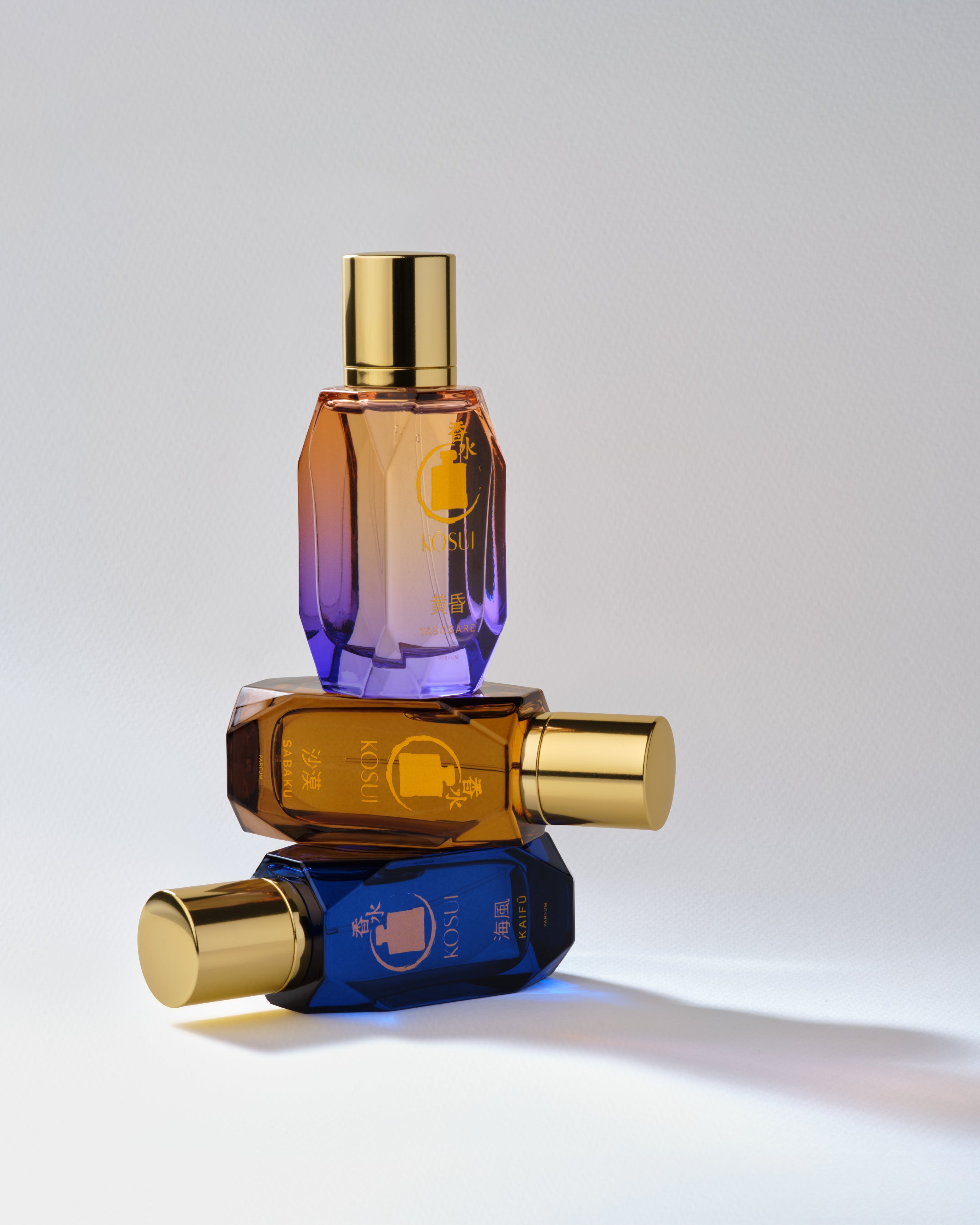 Three gradient perfume bottles stacked on a light gray background