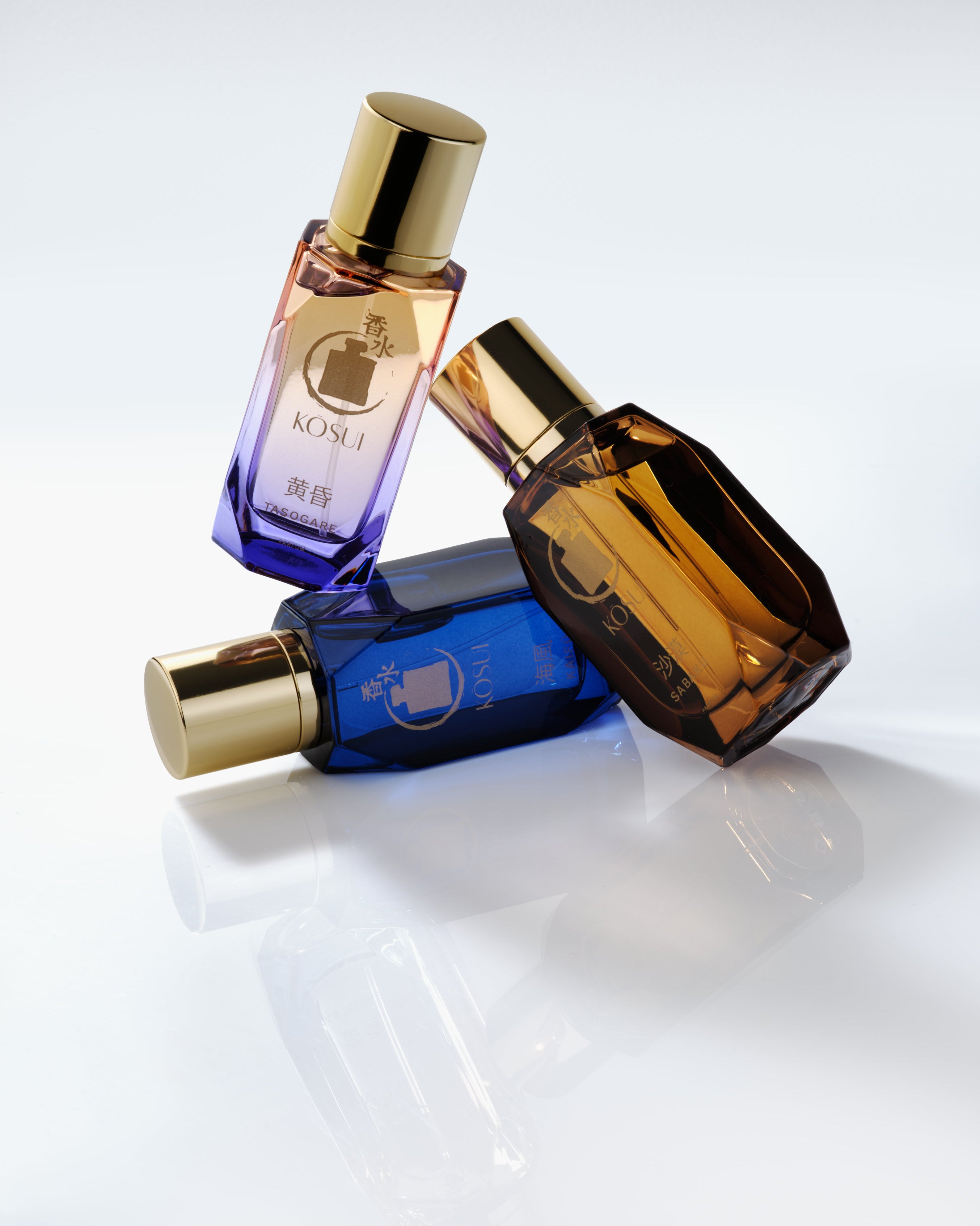 Three perfume bottles with different colored caps on a reflective surface