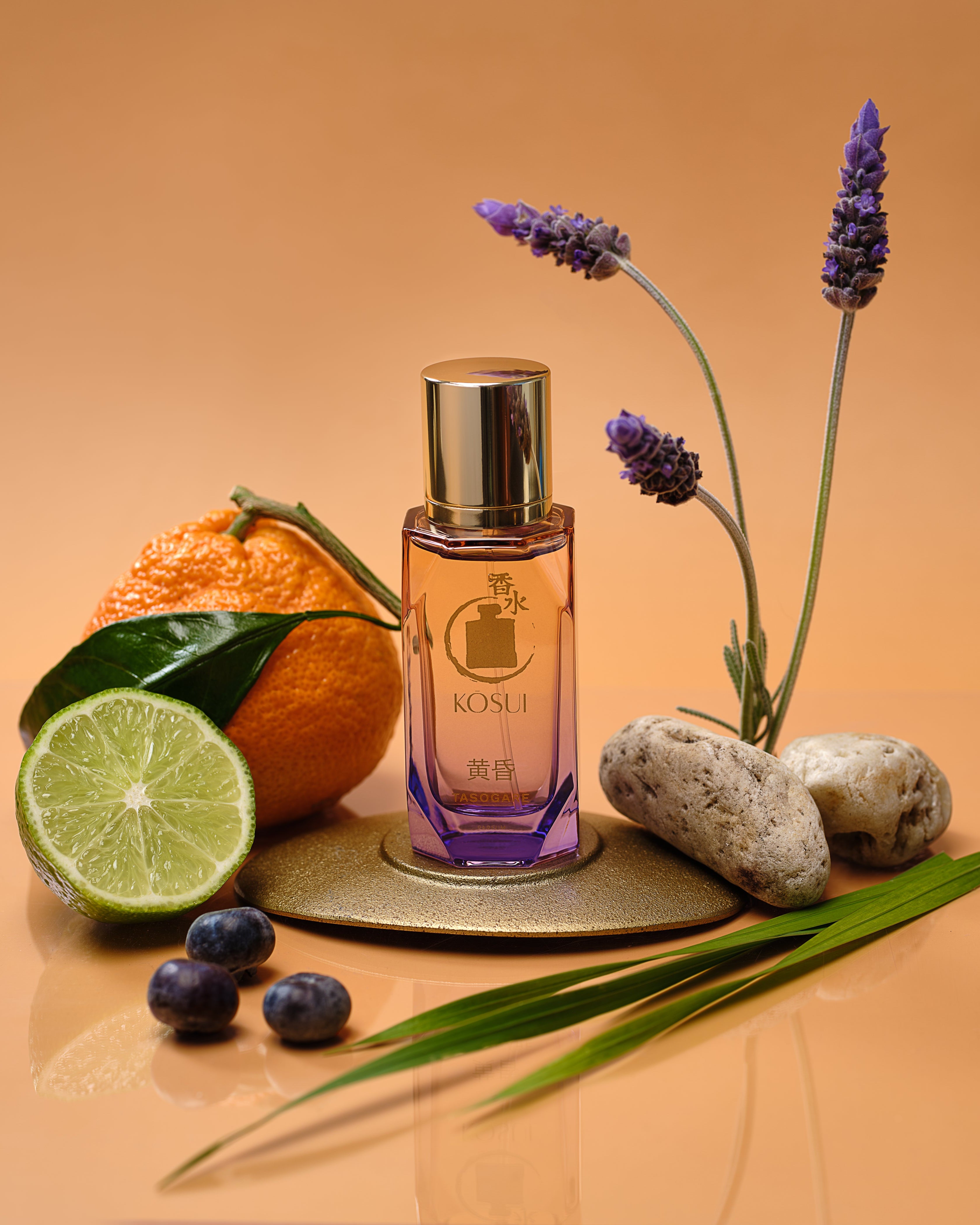 Perfume bottle with lavender, lime, orange, and stones on a peach background