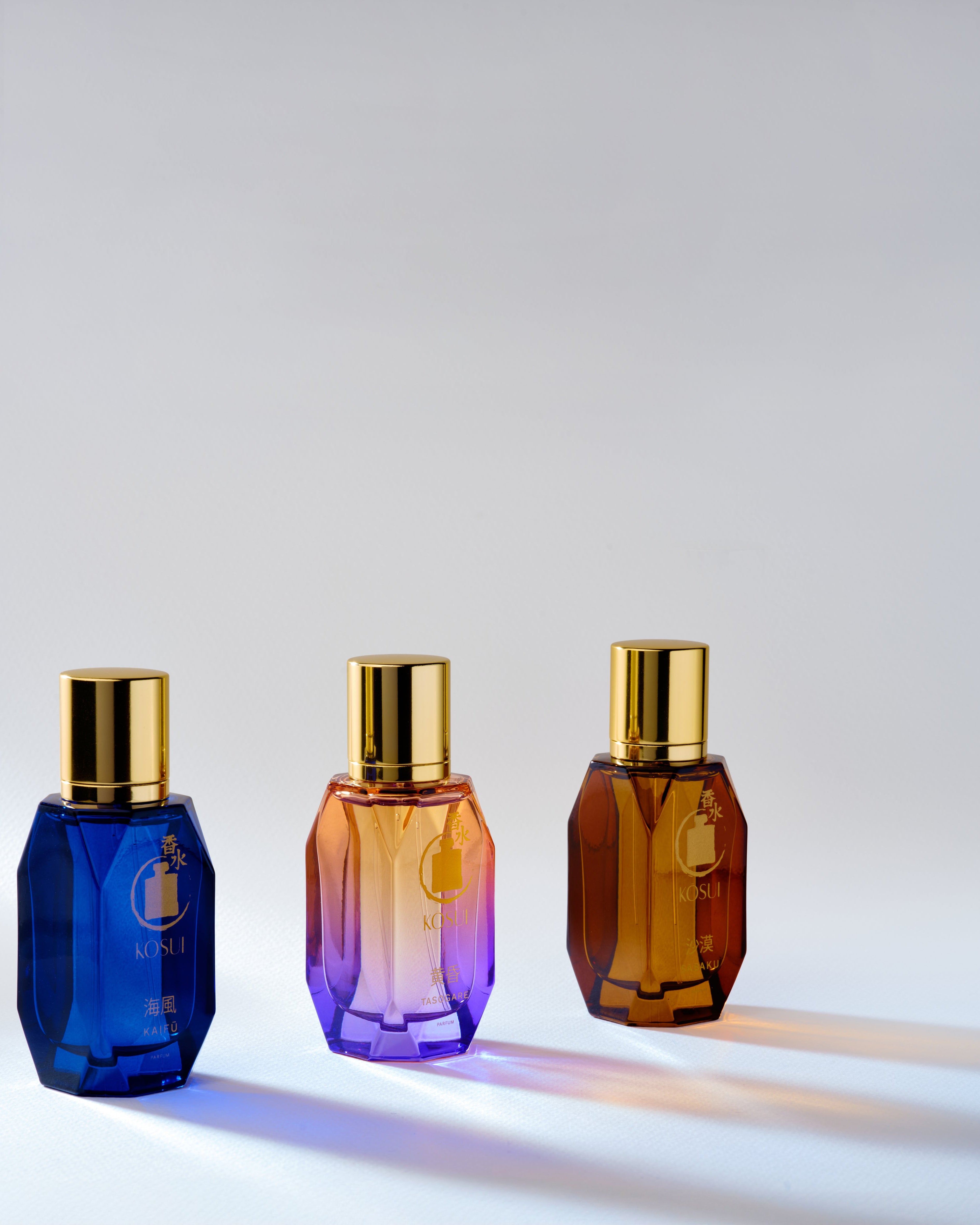 Three gradient perfume bottles with gold caps on a light gray background